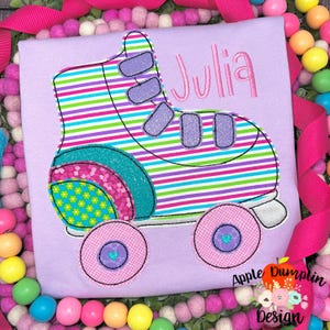May include: A purple t-shirt with a colorful embroidered roller skate and the name "Julia" in pink lettering.