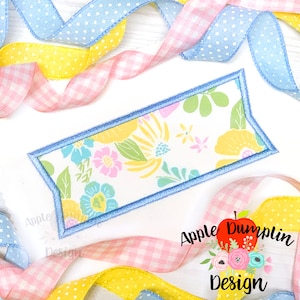 May include: A blue and white floral fabric banner with a scalloped edge. The banner is on a white background with pink and yellow ribbon.