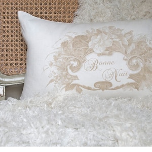May include: A white pillow with a beige floral design and the text "Bonne Nuit" in a decorative font.