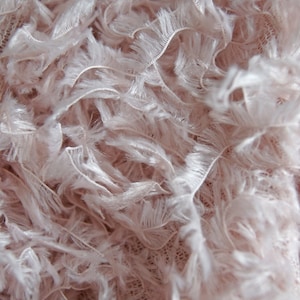 May include: Close-up of a soft, pink fabric with a fluffy, feathery texture. The fabric has a delicate, almost translucent quality.