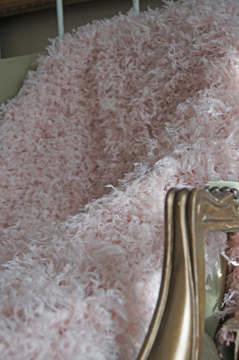 May include: A soft, fluffy pink throw blanket draped over a wooden chair. The blanket is made of a fuzzy, faux fur material.