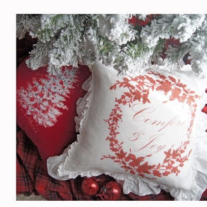 May include: Two decorative pillows with a Christmas theme. One red pillow features a white Christmas tree design with red ornaments. The other is white with a red floral wreath and the words "Comfort & Joy".