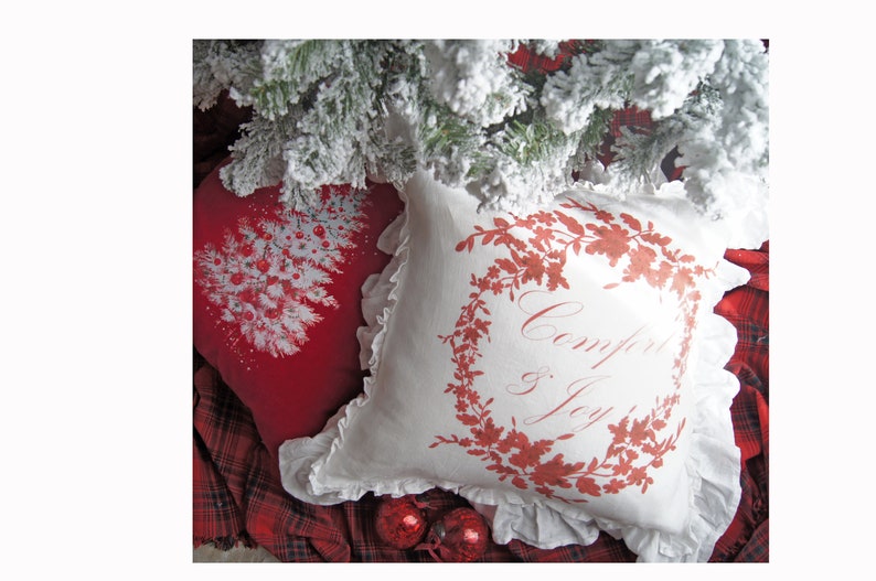 May include: Two decorative pillows with a Christmas theme. One red pillow features a white Christmas tree design with red ornaments. The other is white with a red floral wreath and the words "Comfort & Joy".