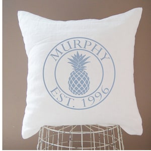 May include: White throw pillow with a blue circle design featuring a pineapple and the text "MURPHY EST. 1996".