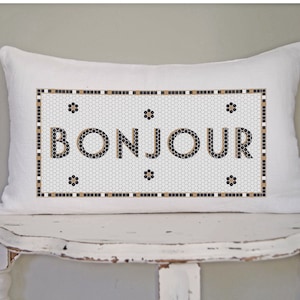 May include: White pillow with a black and gold mosaic design featuring the word "BONJOUR" in a black font.