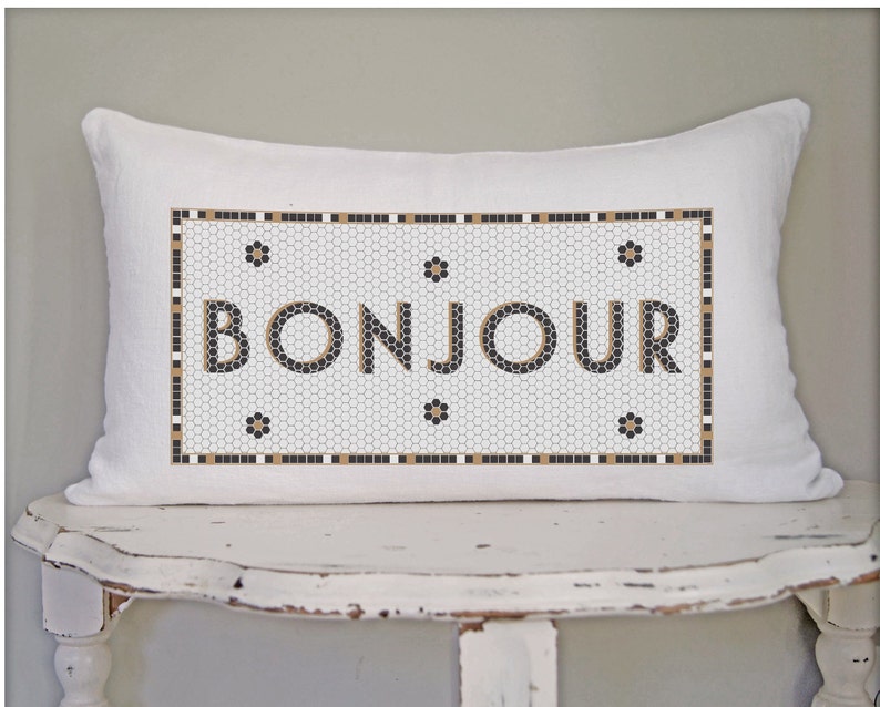 May include: White pillow with a black and gold mosaic design featuring the word "BONJOUR" in a black font.