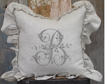 May include: A gray linen pillow with a ruffled edge and an embroidered letter "B" with floral accents.