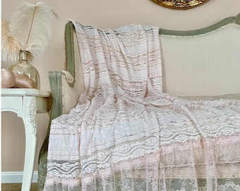 May include: A light pink lace throw blanket draped over a vintage-style sofa. The blanket features intricate floral patterns and a ruffled edge. The sofa has a light green frame and a cream-colored cushion. A decorative mirror hangs on the wall.
