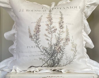May include: White pillow with a ruffled edge and a botanical print featuring a sprig of flowers with the text "J.J. ROUSSEAU BOTANIQUE PARIS" printed on the front.