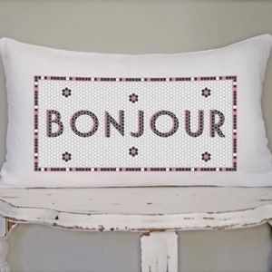 May include: White pillow with a black and white tiled design featuring the word "BONJOUR" in pink lettering.