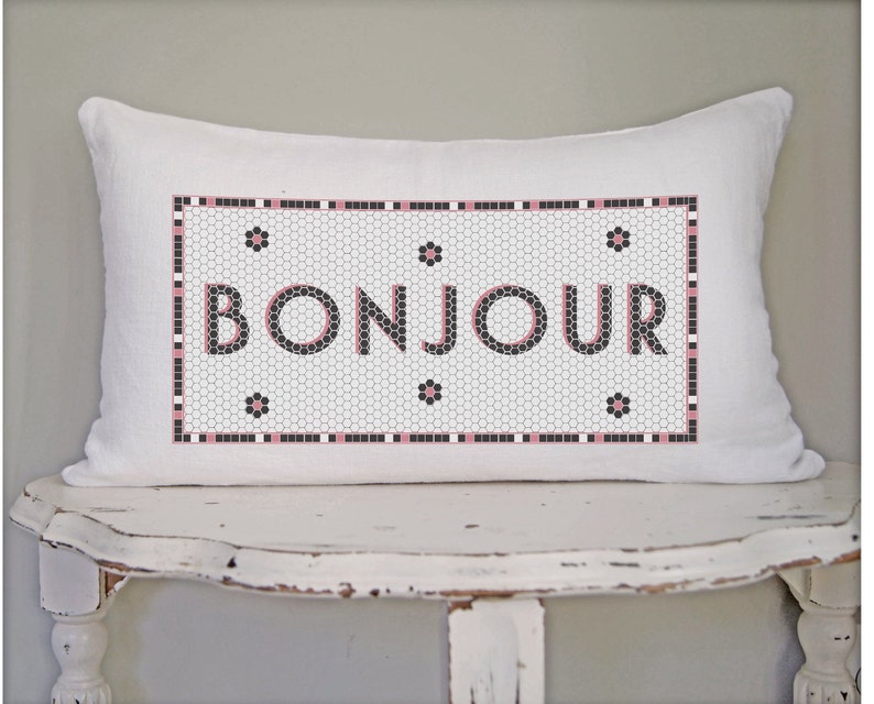 May include: White pillow with a black and white tiled design featuring the word "BONJOUR" in pink lettering.