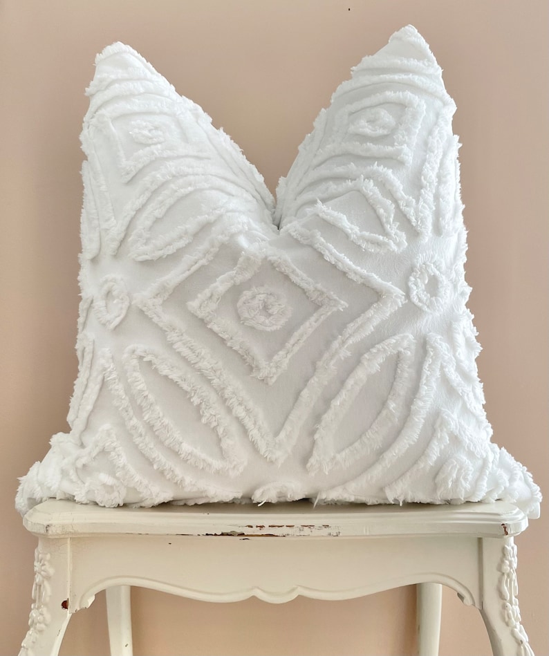 Puede incluir: Almohada blanca de tiro con un patr&oacute;n geom&eacute;trico. La almohada est&aacute; hecha de una tela suave y texturizada y tiene un dise&ntilde;o esponjoso y en relieve.
