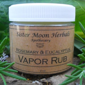 May include: A small glass jar with a white lid, labeled "Sister Moon Herbals Apothecary Rosemary & Eucalyptus Vapor Rub 2 oz."