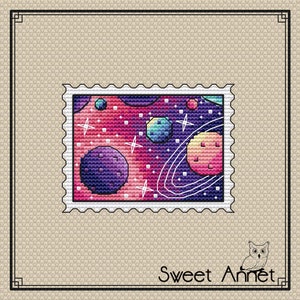 May include: A colorful space-themed cross-stitch pattern with planets, stars, and a galaxy background. The pattern is framed by a white border with a scalloped edge.