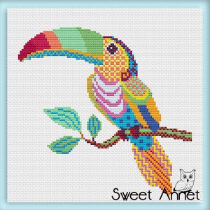 May include: A cross-stitch design depicting a toucan on a branch. The bird has a large, multi-coloured beak and bright feathers in red, green, yellow, and blue. The text "Sweet Annet" is at the bottom of the image.
