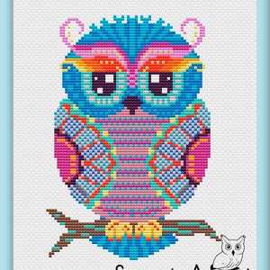 May include: A vibrant cross-stitch owl design in blue, pink, orange, and yellow, perched on a brown branch. The owl features large, square eyes against a white backdrop. The text "Sweet Annet" is displayed at the bottom of the image.