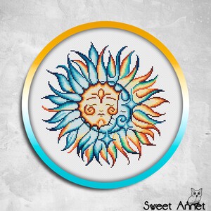 May include: A cross-stitch pattern featuring a stylised sun and moon design. The sun has a face and is surrounded by blue, orange and yellow rays. The moon is crescent-shaped and is behind the sun.