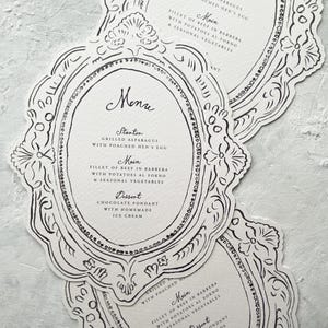 May include: A stack of menu cards with a decorative frame design in black and white. The cards feature the word "Menu" at the top, followed by a list of dishes. The menu includes a starter, main course, and dessert.
