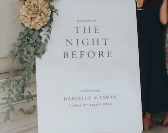 May include: A white sign on an easel with the text "welcome to THE NIGHT BEFORE celebrating DANIELLE & JAMES Friday 6th August 2027". The sign is decorated with flowers and greenery.
