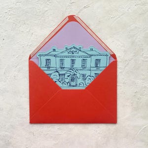 May include: A red envelope with a light purple interior holds a blue illustration of a stately building. The envelope is open, revealing the card with the building design. The background is a textured white surface.