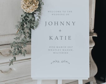 Puede incluir: Señal de bienvenida de boda blanca con el texto "Bienvenido a la boda de Johnny + Katie" y la fecha "25 de marzo de 2017" y la ubicación "Whatley Manor, Wiltshire".