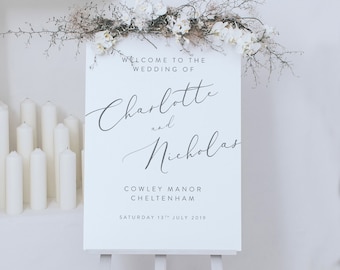 Puede incluir: Señal de bienvenida de boda blanca con texto en caligrafía que dice "Bienvenido a la boda de Charlotte y Nicholas, Cowley Manor Cheltenham, sábado 13 de julio de 2019".
