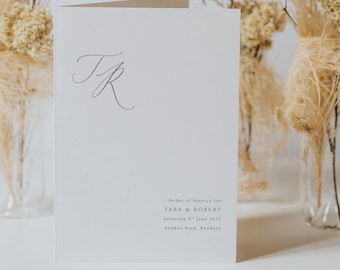 May include: A white card with the text "Order of Service for TARA & ROBERT Saturday 4th June 2022 Aynhoe Park, Banbury" and the initials "T&R" in cursive.