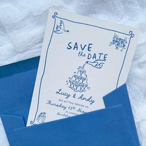 May include: Save the date card with a blue and white design. The card features a hand pouring champagne into a tower of glasses. The text on the card reads "Save the Date", "Lucy & Andy", "Are getting married on", "Thursday 13th May", "In London", and "Invitations".