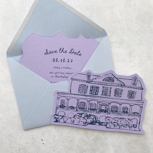 May include: A light blue envelope with a lavender insert featuring the text "Save the Date" and a date. A lavender card with a house illustration is next to the envelope. The card reads "Haley & Nathan are getting married in Charleston."