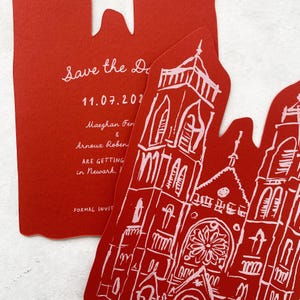 May include: Red wedding invitation with a church illustration and the text "Save the Date" and event details. The invitation is die-cut with a unique shape. The text includes the date, names, and location.