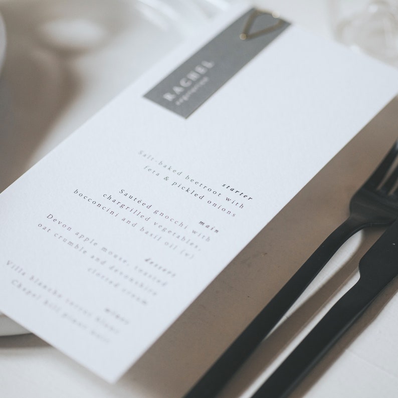 May include: A white menu with the name "Rachel" printed on a gray tag. The menu lists a starter of salt-baked beetroot with feta and pickled onions, a main of sauteed gnocchi with chargrilled vegetables, bocconcini and basil oil, and a dessert of Devon apple mousse, toasted oat crumble and clotted cream.