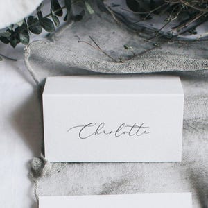 Puede incluir: Tarjeta de lugar blanca con el nombre Charlotte escrito en cursiva.