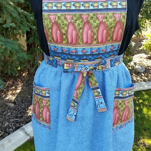 May include: A blue and white kitchen towel apron with a cat and coffee cup design. The apron has two pockets and a tie at the waist.