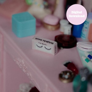Könnte beinhalten: Ein kleiner Kasten mit Wimpern auf einem rosa Schminktisch. Der Kasten ist weiß mit schwarzem Text, der "Top Quality" und "Brichida Lash" lautet.