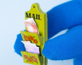 Puede incluir: Un pequeño organizador de correo verde lima con tres compartimentos, que contiene papeles de colores. La palabra "MAIL" está impresa en negro en la parte superior. Cada bolsillo está decorado con un diseño floral en rojo, amarillo y verde.