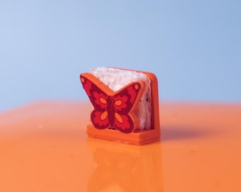 Puede incluir: Un servilletero naranja con un diseño de mariposa roja. La mariposa tiene un patrón detallado y está centrada en el soporte. El soporte está lleno de servilletas blancas. El fondo es un degradado de naranja y azul.