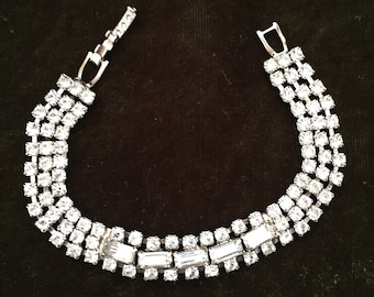 May include: A silver bracelet with a row of clear rhinestones. The bracelet has a simple clasp.