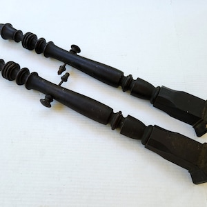 May include: Two dark brown wooden furniture legs with a decorative, fluted design. The legs have a square base and a rounded top with a threaded section.