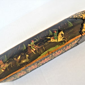 Peut inclure: Longue boîte en bois noir avec couvercle, ornée d'une scène peinte à la main de personnages à cheval chassant des cerfs. La boîte est décorée de motifs floraux roses et jaunes, et les bords sont dorés.