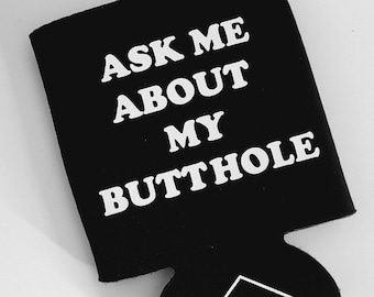 Può includere: Isolante per bevande nero con testo bianco che recita "ASK ME ABOUT MY BUTTHOLE". La parte inferiore dell'isolante ha una forma ritagliata e un piccolo triangolo bianco con la parola "KUNTY".