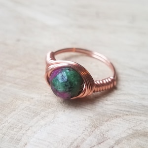 May include: A copper wire wrapped ring with a green and pink gemstone.