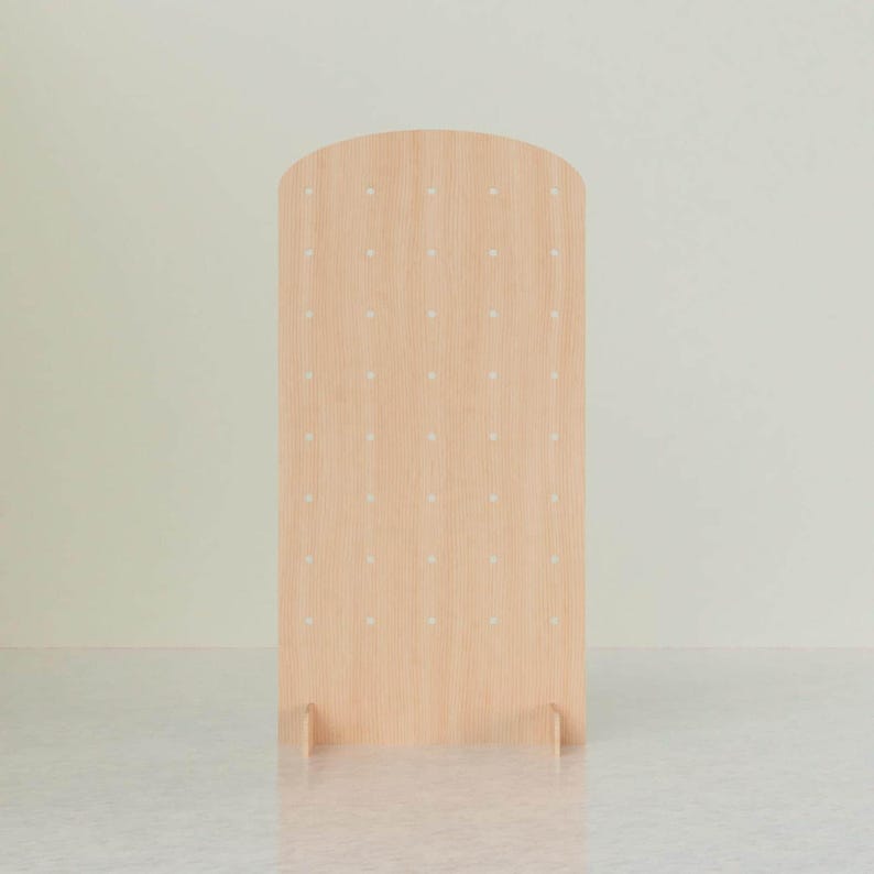 A light wood arched pegboard display stand with evenly spaced holes, standing upright on two support feet, centered against a light background.