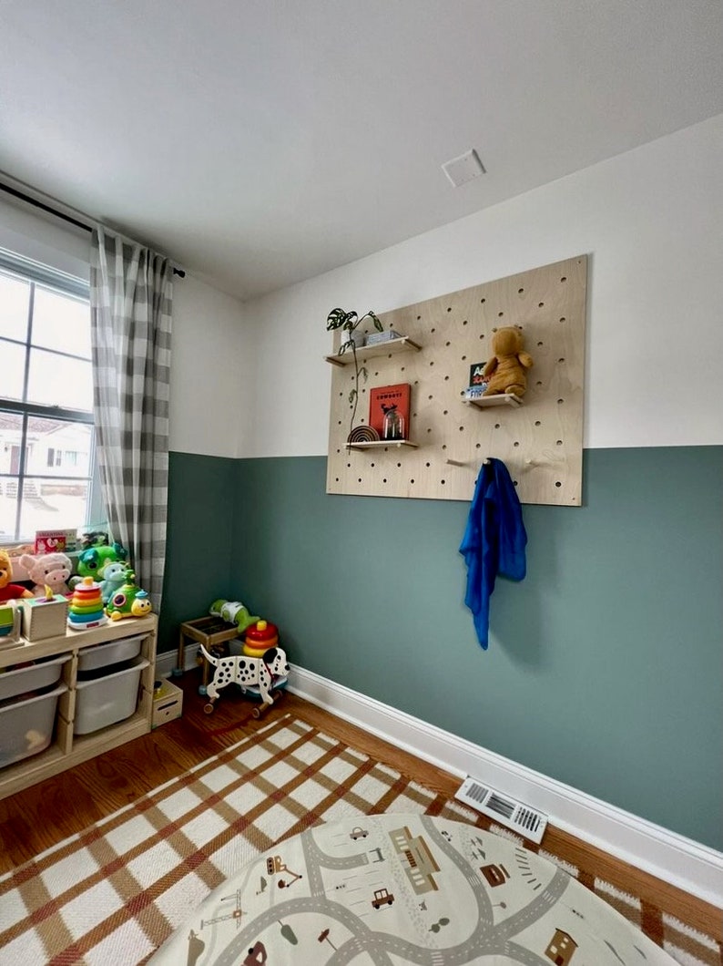 Puede incluir: Un tablero perforado rectangular grande de madera clara montado en una pared, con m&uacute;ltiples orificios circulares para estantes ajustables. El tablero sostiene estantes peque&ntilde;os de madera con libros, una planta peque&ntilde;a y un peluche.