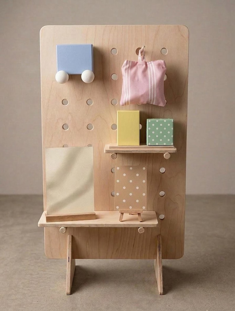 A light wood pegboard display stand with various small, colorful decorative items and shelves, including a blue block, pink striped bag, and yellow box.