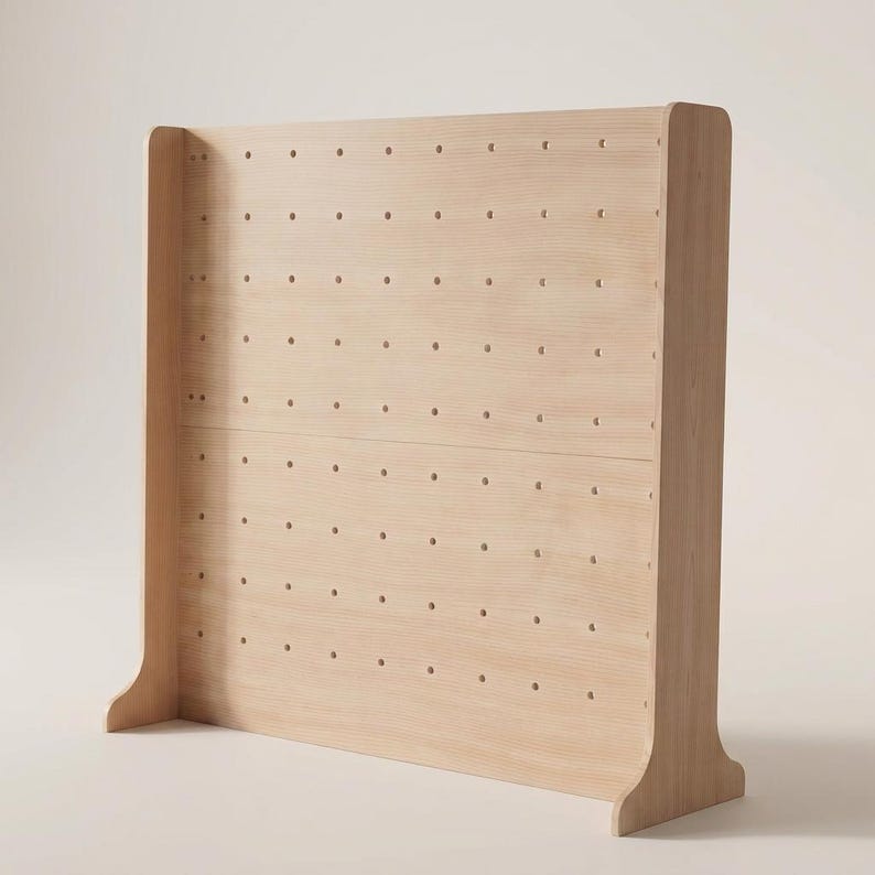 May include: A light-colored wooden pegboard display stand featuring a rectangular panel with a grid of evenly spaced circular holes. The structure includes two side supports that extend outward at the base to provide stability for the unit.