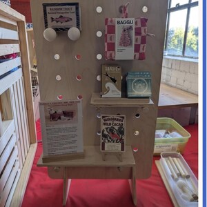 A light wood pegboard display stand with various small products, including packaged goods and informational cards, displayed on shelves and pegs.