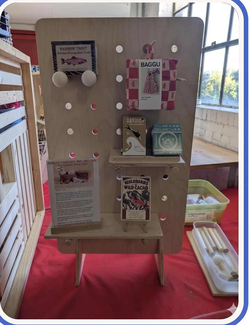 A light wood pegboard display stand with various small products, including packaged goods and informational cards, displayed on shelves and pegs.