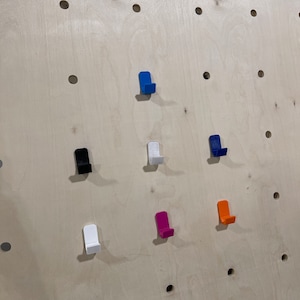 May include: A wall with seven different colored hooks. The hooks are all the same shape and size, but they are different colors. The colors are blue, black, white, pink, orange, and two different shades of blue.