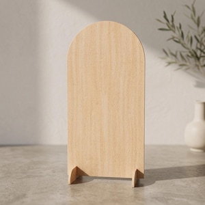 May include: A light-coloured wooden sign with a smooth, arched top and a flat rectangular base. The sign features a visible natural wood grain pattern throughout its surface and is supported by two small, perpendicular wooden feet at the bottom.