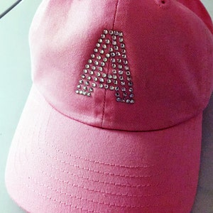 May include: A pink baseball cap with a large letter A made of rhinestones on the front.